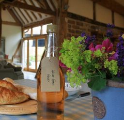 A kitchen table with a bottle of drink labeled Whites Farm Perry croissants bread and a flower arrangement at Whites Farm Barn Ledbury