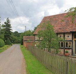 A country road with a brick and timber house with a tiled roof and wooden fence at Whites Farm Barn in Ledbury