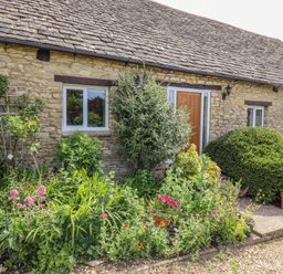 A stone cottage exterior with a garden and plants at Pheasant Cottage in Minster Lovell