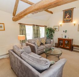 A sitting room with two grey sofas a glass coffee table wooden furniture and exposed wooden beams at Pheasant Cottage in Minster Lovell