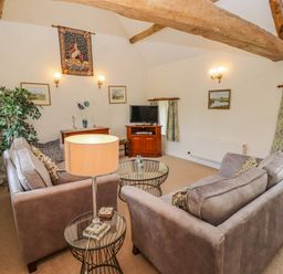 A living room with two sofas a glass coffee table a lamp and wooden beams at Pheasant Cottage in Minster Lovell