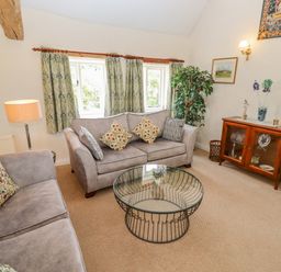 A living room with two sofas a glass coffee table a wooden cabinet and a potted plant at Pheasant Cottage in Minster Lovell
