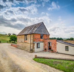 A barn-style building with brick and stone walls on a gravel driveway in a rural landscape at Top Barn in Chipping Norton