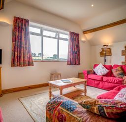 A living room with red sofas, wooden coffee table, patterned curtains, TV on wooden cabinet and exposed wooden beams at Top Barn in Chipping Norton