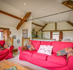 A living room with red sofas wooden beams and an open kitchen and dining area at Top Barn in Chipping Norton