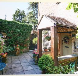 A stone patio with a covered wooden porch door surrounded by potted plants and hedges at Pike Cottage in Stow-On-The-Wold