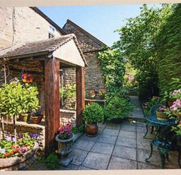 A garden patio with stone walls potted plants and a small metal table with chairs at Pike Cottage in Stow-On-The-Wold