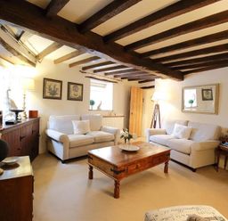 A living room with wooden beams on the ceiling two white sofas a wooden coffee table and a floor lamp at Pike Cottage in Stow-On-The-Wold