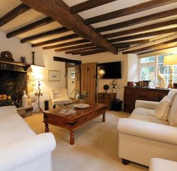 A living room with wooden ceiling beams a stone fireplace two beige sofas and a wooden coffee table at Pike Cottage in Stow-On-The-Wold