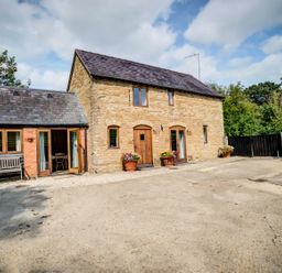 Exterior view of a stone and brick house with wooden doors and windows and flower pots at Little Barn in Ascott near Chipping Norton