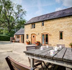 A stone cottage with wooden doors and windows and outdoor table with mugs at Little Barn in Ascott near Chipping Norton