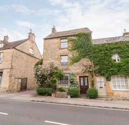 A stone house with greenery on the facade and two doors next to a street at Benfield in Stow-on-the-Wold