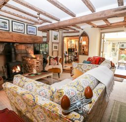 A living room with patterned sofas a wood burning stove and exposed wooden beams at Benfield in Stow-on-the-Wold