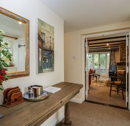 A hallway with a wooden table and decorative items leading to a living room with chairs and a fireplace at Anvil Cottage in Chipping Norton