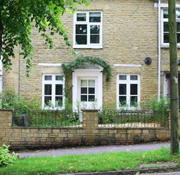 Front of a stone house with white framed windows and door with plants and a tree in front at Hare House in Chipping Norton