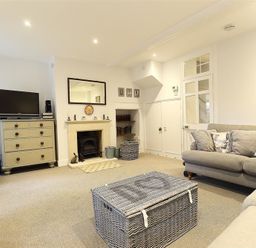 A living room with a sofa a chest of drawers a TV fireplace and a wicker coffee table at Hare House in Chipping Norton