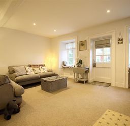 A living room with sofas cushions a wicker coffee table a lamp and windows with seating at Hare House in Chipping Norton