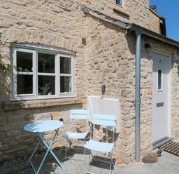 A stone house exterior with a white door number 2 and a small blue table with two blue chairs outside at Batemans in Nailsworth
