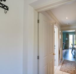 A hallway with white doors a rug on the tiled floor and a view into a room with dark wooden flooring at Batemans in Nailsworth