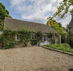 A stone building with a tiled roof and climbing plants near a gravel area at Hazel Manor Wing in Painswick