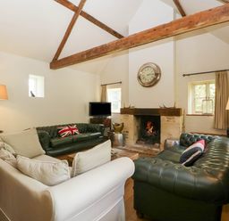 A living room with leather sofas a fireplace and wooden beams at Hazel Manor Wing in Painswick