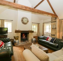 A living room with two green leather sofas a beige sofa a wooden coffee table a fireplace and a television at Hazel Manor Wing in Painswick