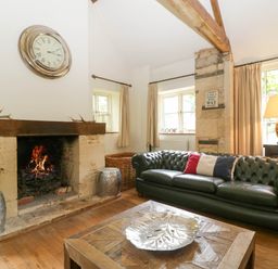 A living room with a fireplace a clock a leather sofa and a wooden coffee table at Hazel Manor Wing in Painswick