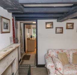 A living room with floral sofa cushions a fireplace and framed pictures on the wall at Newbury Cottage in Bourton-On-The-Water