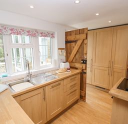A kitchen with wooden cabinets a sink toaster and a wooden door at Newbury Cottage in Bourton-On-The-Water