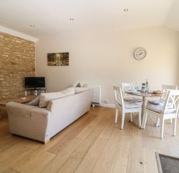 A living room with a beige sofa a wooden coffee table a small television and a dining table with four chairs at Saddlebacks Barn in Burford