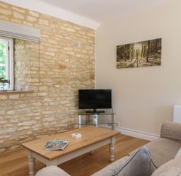 A living room with a stone wall a window a coffee table a sofa a television and a forest picture on the wall at Saddlebacks Barn in Burford