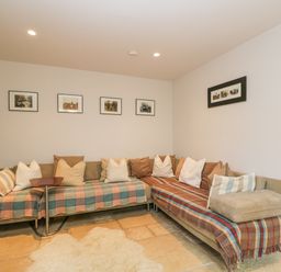 A living room with a sectional sofa covered in blankets and cushions and framed pictures on the wall at The Lodge in Coln St Aldwyns