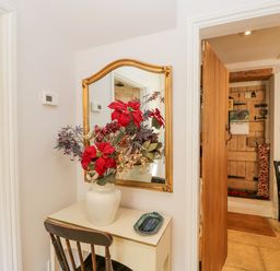 A small table with a vase of flowers and a mirror above it next to an open wooden door in a hallway at The Lodge in Coln St Aldwyns