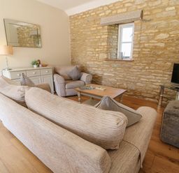 A living room with sofas a coffee table a television on a stand and a sideboard against a stone wall at Ewecub Barn in Burford