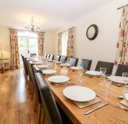 A dining room with a long wooden table set with plates and glasses at South Hill Farmhouse in Stow-On-The-Wold