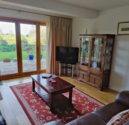 A living room with a wooden coffee table and glass cabinet next to large sliding doors opening to a garden at 5 Burford Mews in Burford