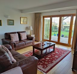 A living room with two brown leather sofas a wooden coffee table a red patterned rug framed pictures on the wall and glass doors leading outside at 5 Burford Mews in Burford