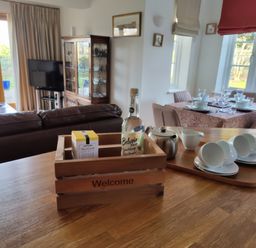 A kitchen counter with a wooden crate labeled welcome holding a bottle and a box a tray with teacups a teapot and a creamer in a living and dining room at 5 Burford Mews in Burford