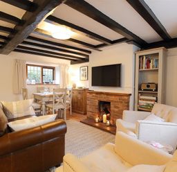 A living room with a brown leather sofa white armchairs dining table and brick fireplace at One Masons Court in Stratford upon Avon