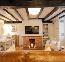 A living room with exposed beams a brick fireplace a TV a dining table and chairs at One Masons Court in Stratford upon Avon
