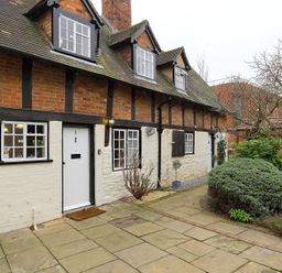 A brick and timber framed house with white doors and windows and a garden with shrubs and trees at One Masons Court in Stratford upon Avon
