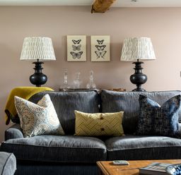 A living room with a gray sofa with patterned cushions two black lamps with patterned shades and butterfly artwork on the wall at Orchard House in Stow-On-The-Wold