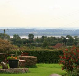 A garden with chairs and a flower pot overlooking trees and hills at The Piggery in Lydney