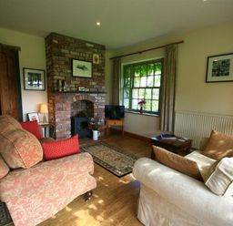 A living room with a brick fireplace couches and a window with curtains at The Piggery in Lydney