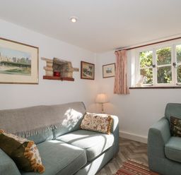 A sitting room with two sofas a lamp paintings on the wall and a window with curtains at Mayfly Cottage Coln St Aldwyns near Bibury