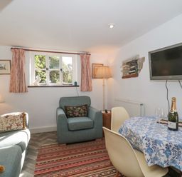 A living room with sofa armchair table with blue floral tablecloth and wall mounted TV at Mayfly Cottage Coln St Aldwyns near Bibury