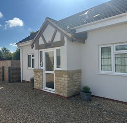 The exterior of a white house with a stone and wood porch entrance and gravel driveway at Old Groom's Cottage in Minster Lovell