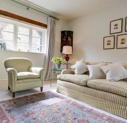 A living room with an armchair, a striped sofa with cushions, a rug, a side table with flowers and a lamp, and framed pictures on the wall at The Old Dairy in Shilton