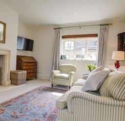 A living room with a striped sofa armchair fireplace and television at The Old Dairy in Shilton