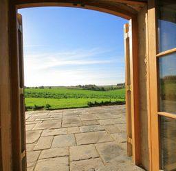 A stone patio outside open wooden double doors with a view of green fields and blue sky at Calcot Peak Barn in Bibury near Northleach
